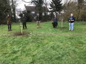 Five people stood by newly planted trees on the playing field